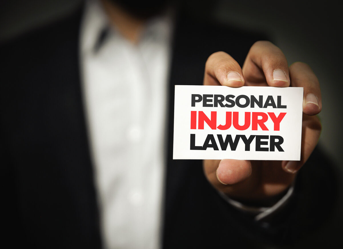 a black suited man showing "personal injury lawyer" card in hand.