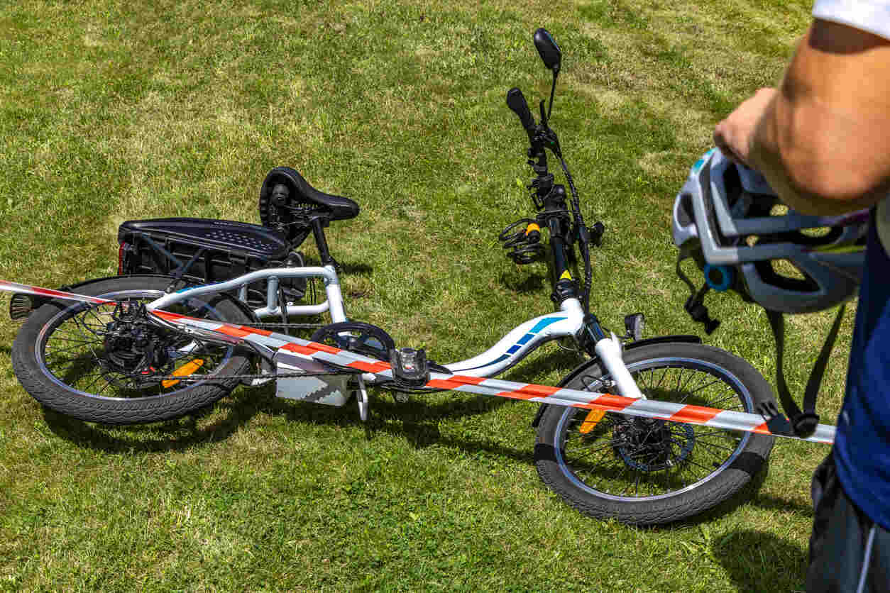 E-bike lying on the grass, cordoned off with red and white tape, suggesting a recent accident.