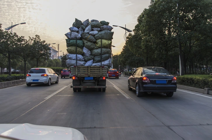 An overloaded truck is seen from behind, carrying unstable pile of cargo on a multi-lane road, illustrating the dangers that can lead to an overloaded truck accident.