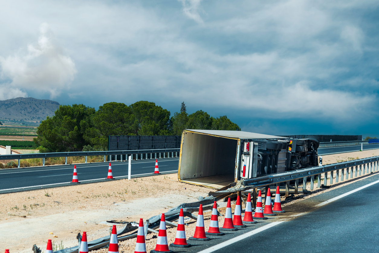 An overturned semi-truck trailer on the side of a highway, surrounded by orange traffic cones, representing a truck rollover accident in Denver.