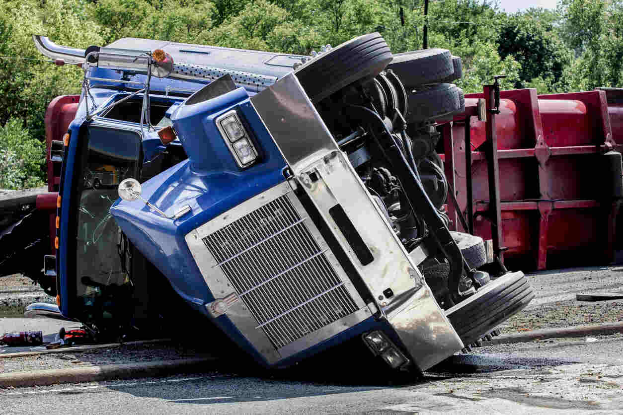 A large blue and red semi-truck overturned on its side, illustrating a severe jackknife accident in Denver.